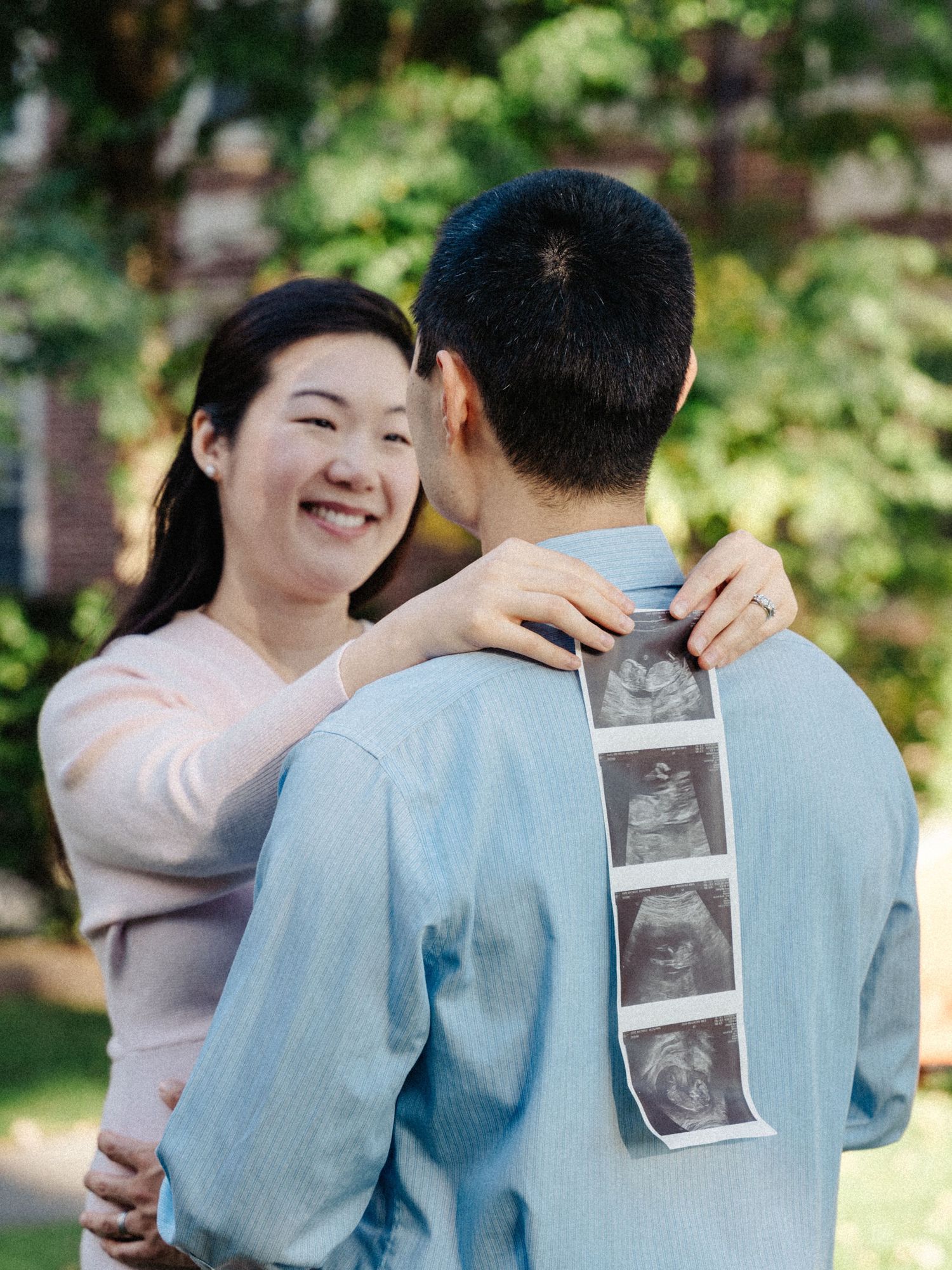 A couple embraces outdoors while displaying ultrasound photos at Harvard campus.