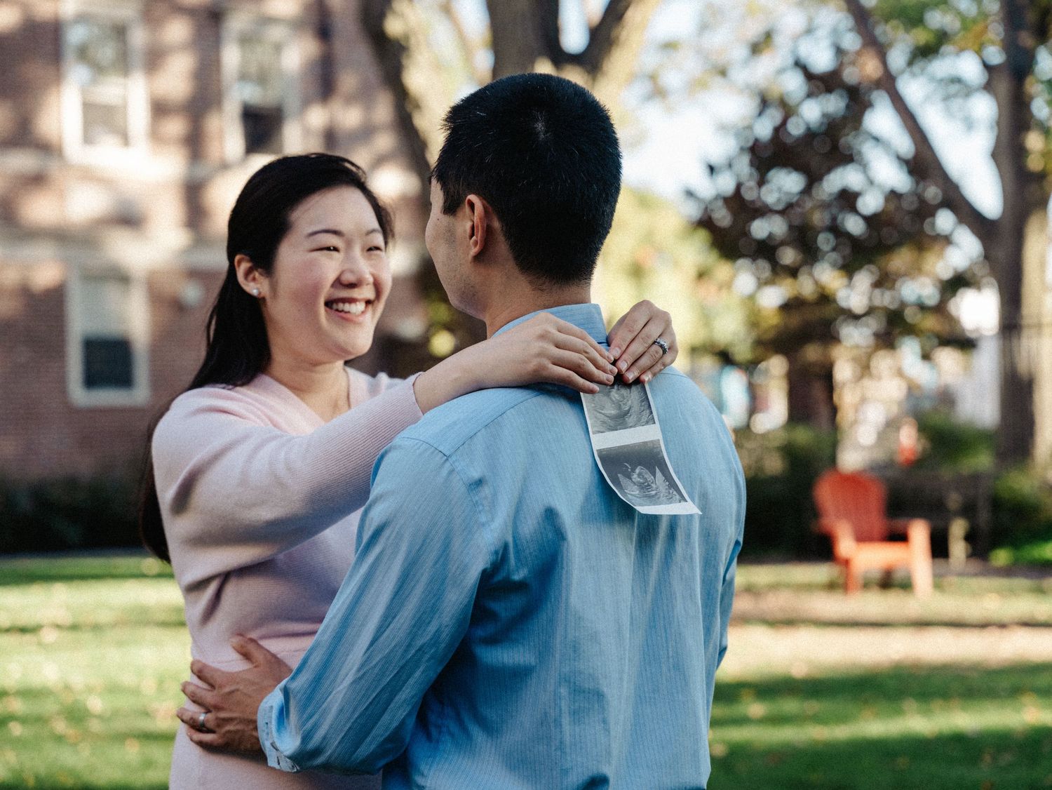 A couple shares a joyful moment while holding ultrasound photos outdoors at Harvard campus.