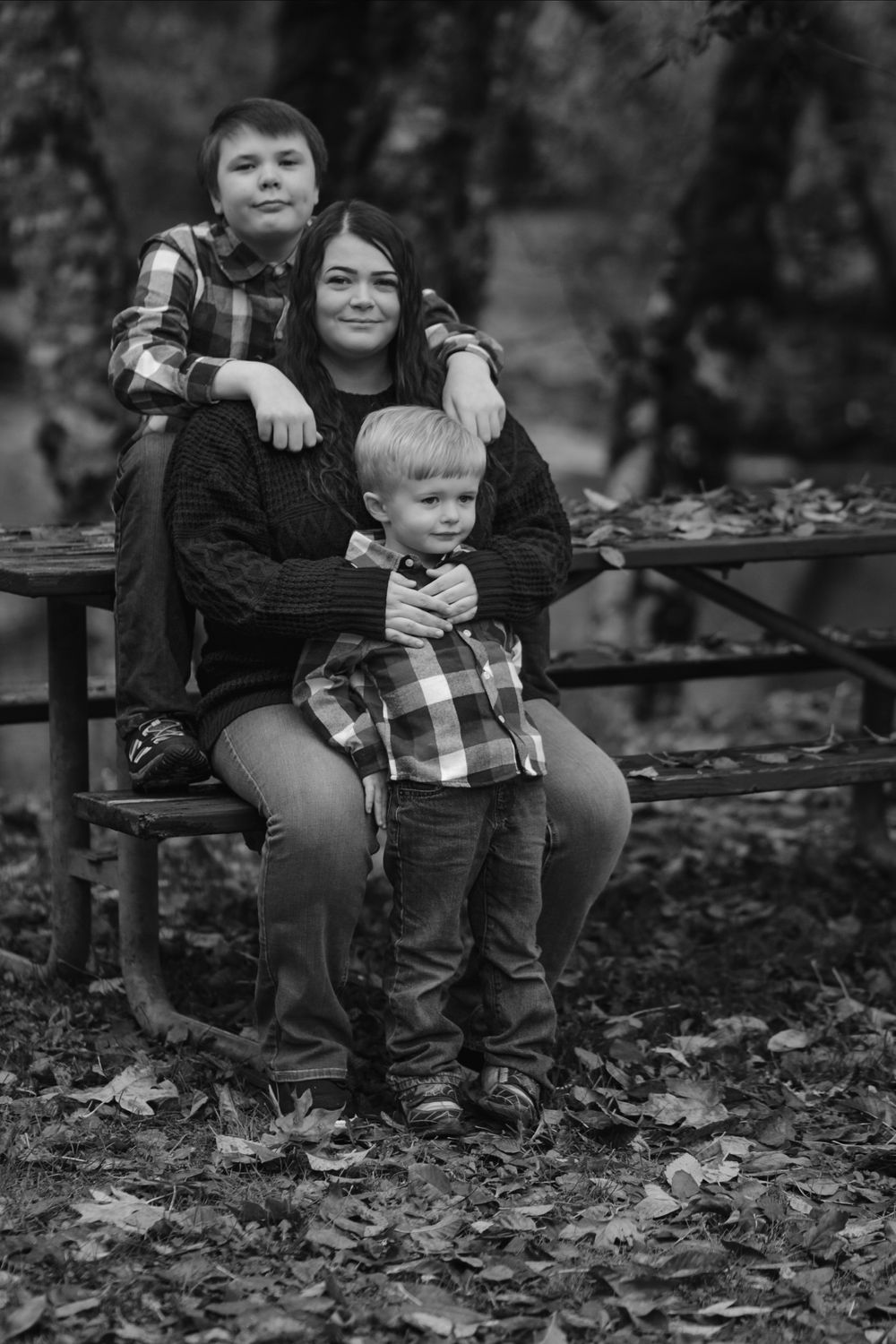 Black and white family portrait of mother sitting with two sons on park bench.