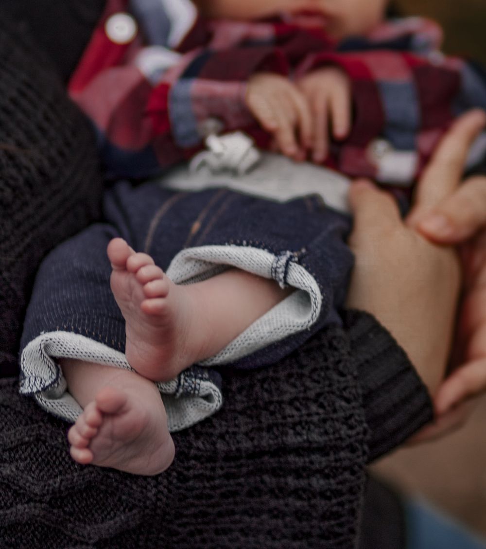 Close-up of tiny newborn baby feet peeking out from a cozy navy sweater onesie.
