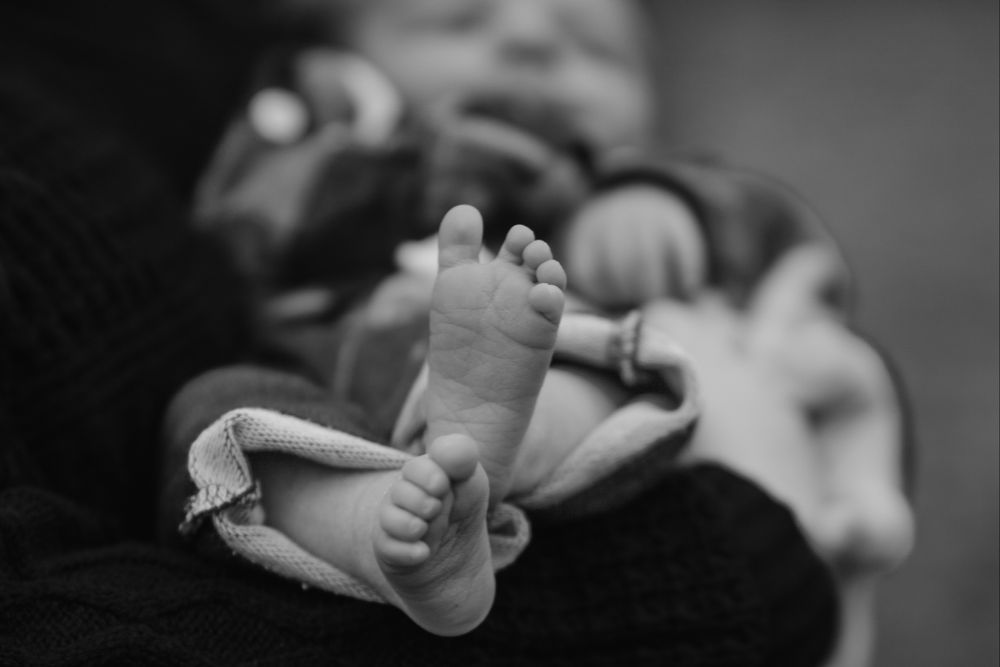 Black and white close-up of newborn baby tiny feet being held by mother.