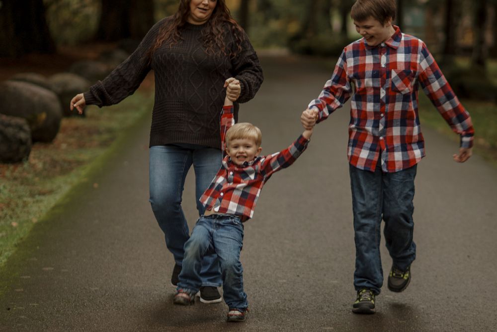 Mother and two sons walking hand in hand down a tree-lined path in an autumn park.