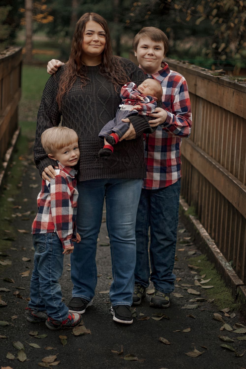 Mother with three children including newborn baby posing on a wooden bridge in autumn park.