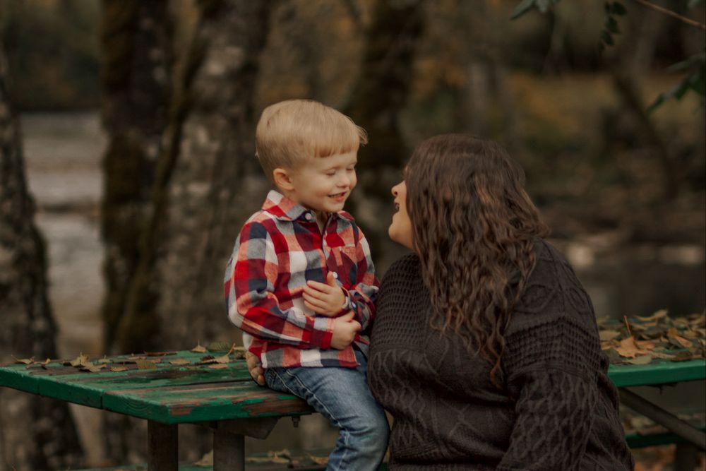 Mother and young blonde son sharing a sweet moment on a park bench surrounded by fall foliage.