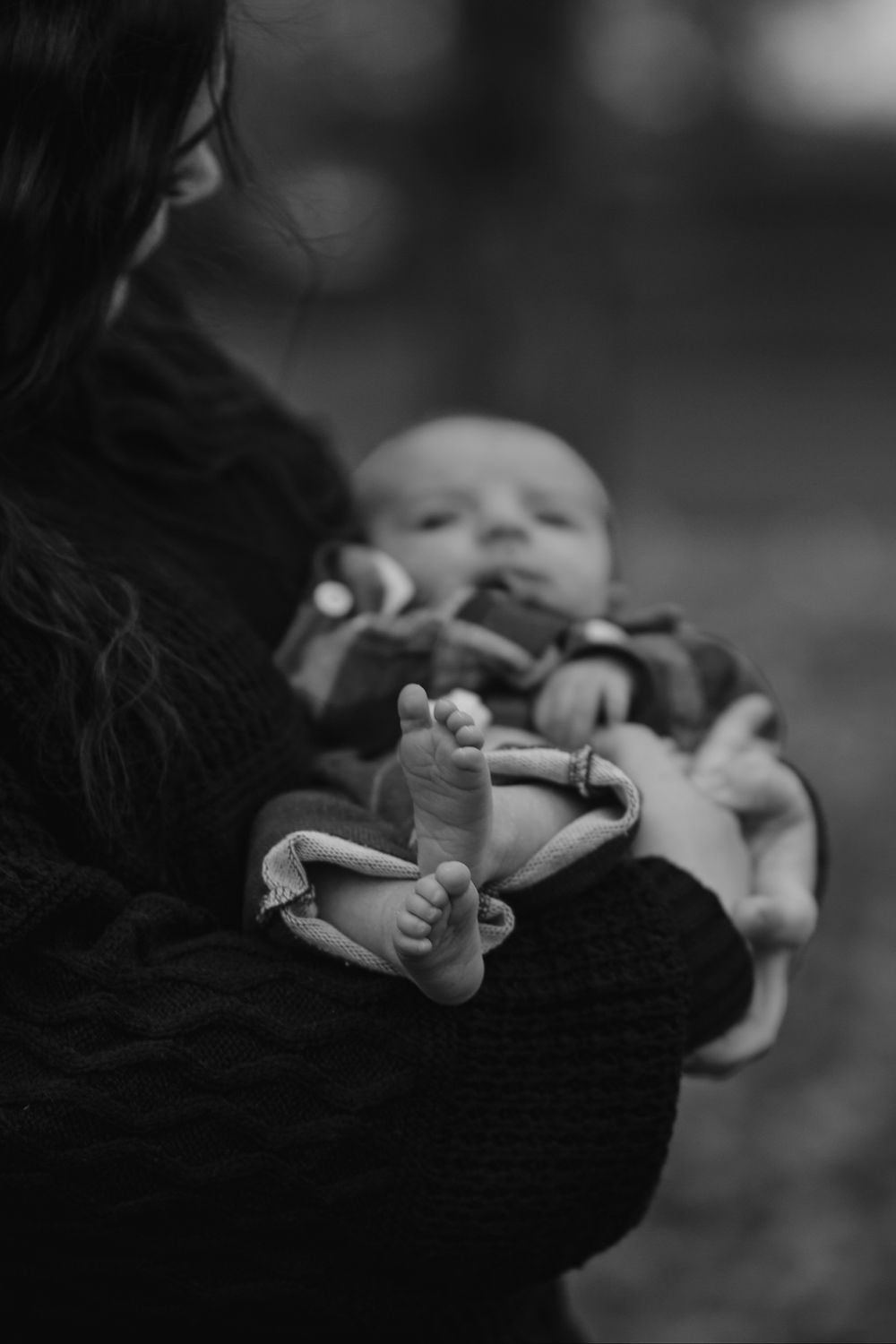 Black and white close-up of mother holding newborn baby in arms outdoors in fall.