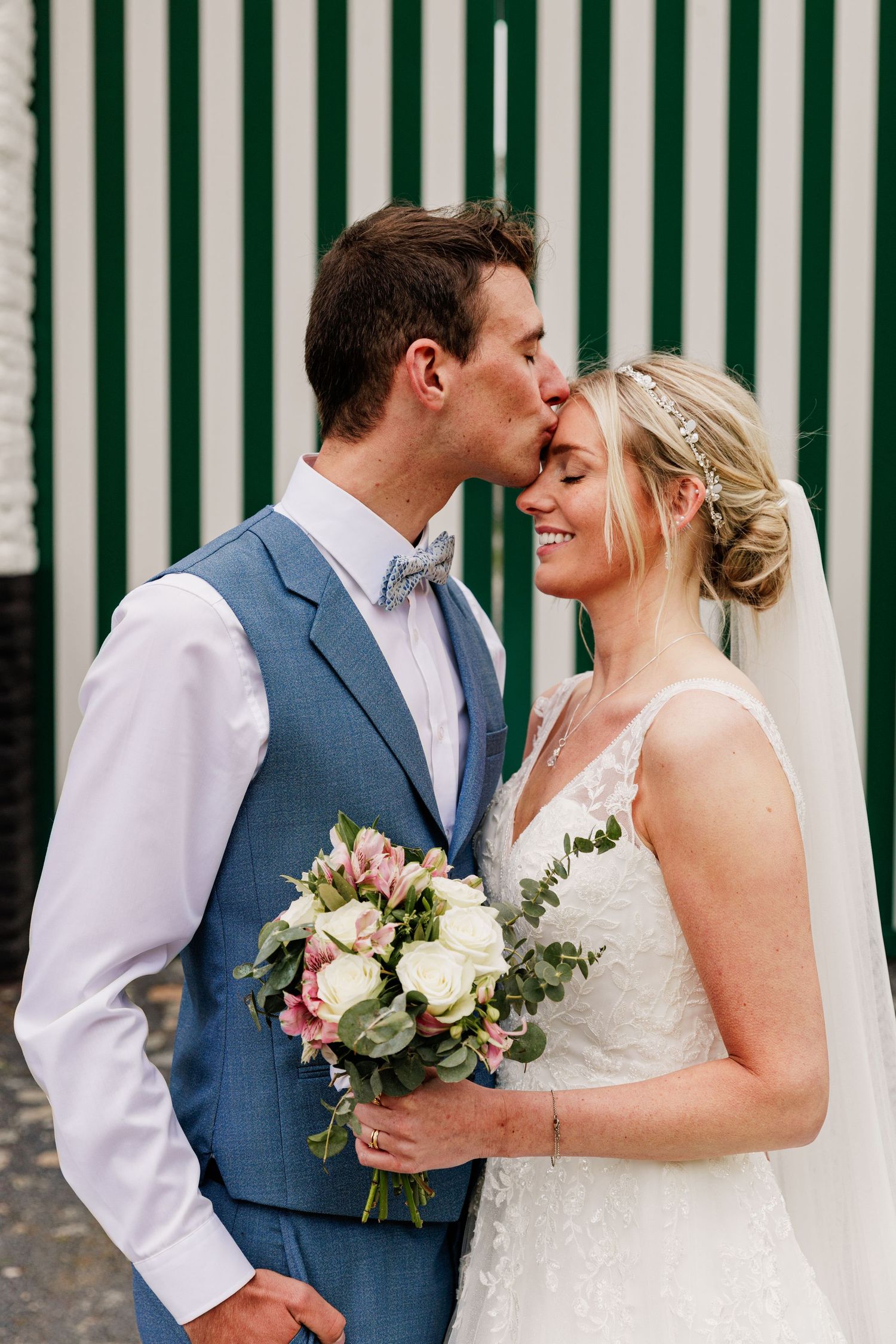 Romantic wedding couple shares intimate moments against green and white striped backdrop.
