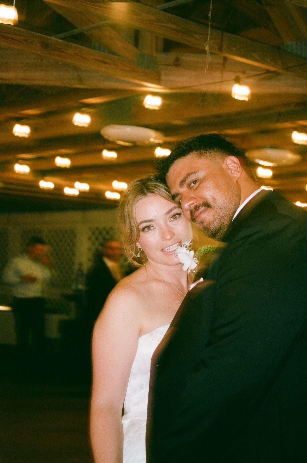A bride and groom share a tender moment on the dance floor at their wedding reception under warm glowing lights.
