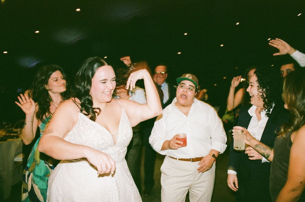 Bride in white lace gown dancing joyfully with guests at a lively wedding reception celebration.