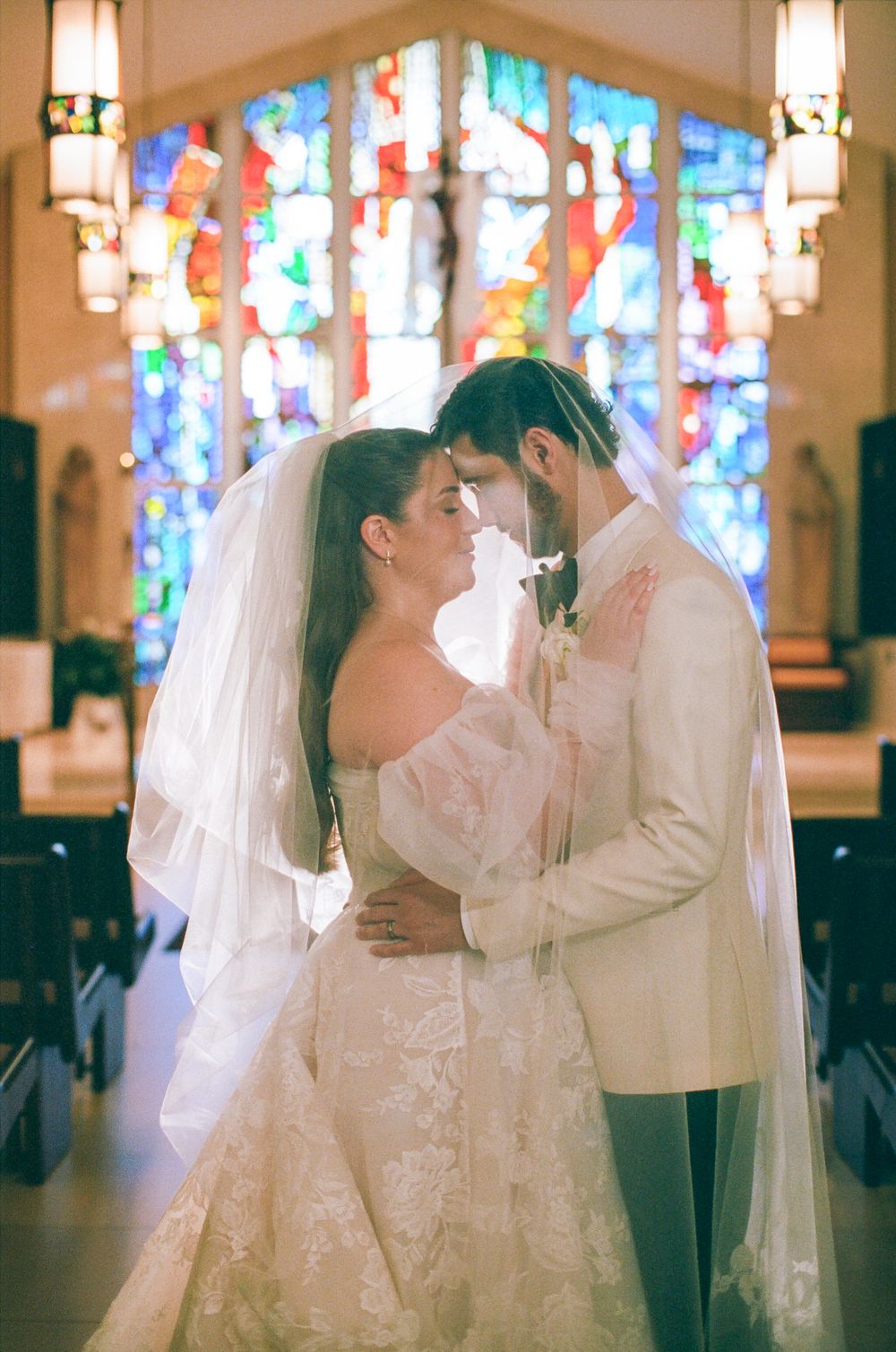Bride and groom share an intimate moment in a church with stunning stained glass windows backdrop on their wedding day.