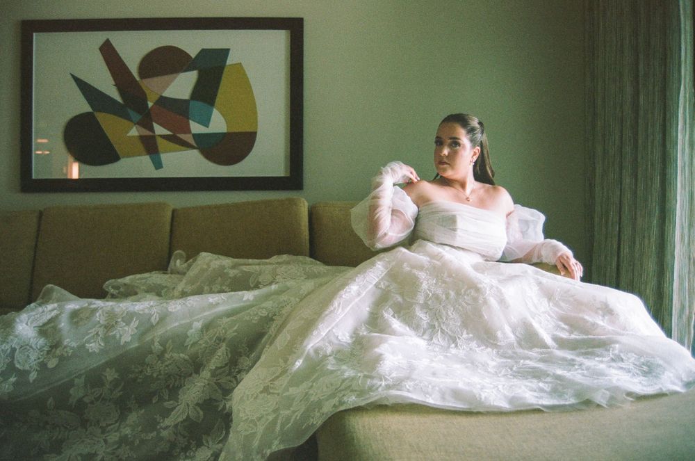 Bride in a white ball gown wedding dress sitting on a green sofa with abstract art on the wall behind her.