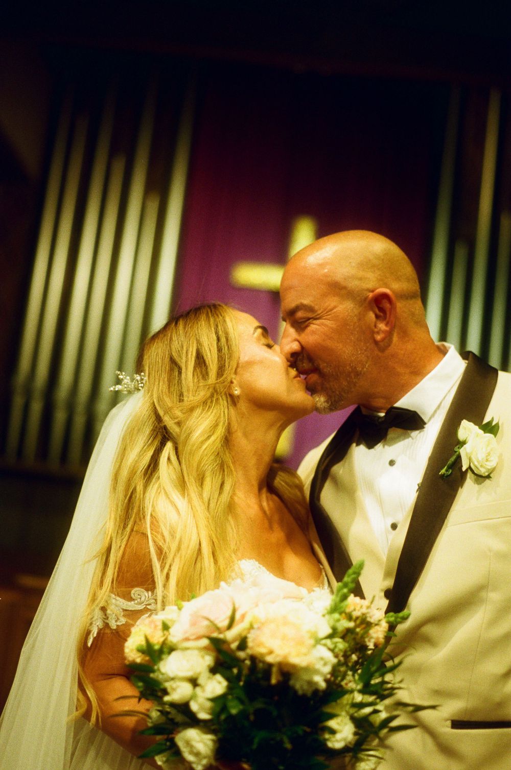 A bride in a white gown holding a floral bouquet shares a romantic moment at the altar during a wedding ceremony.
