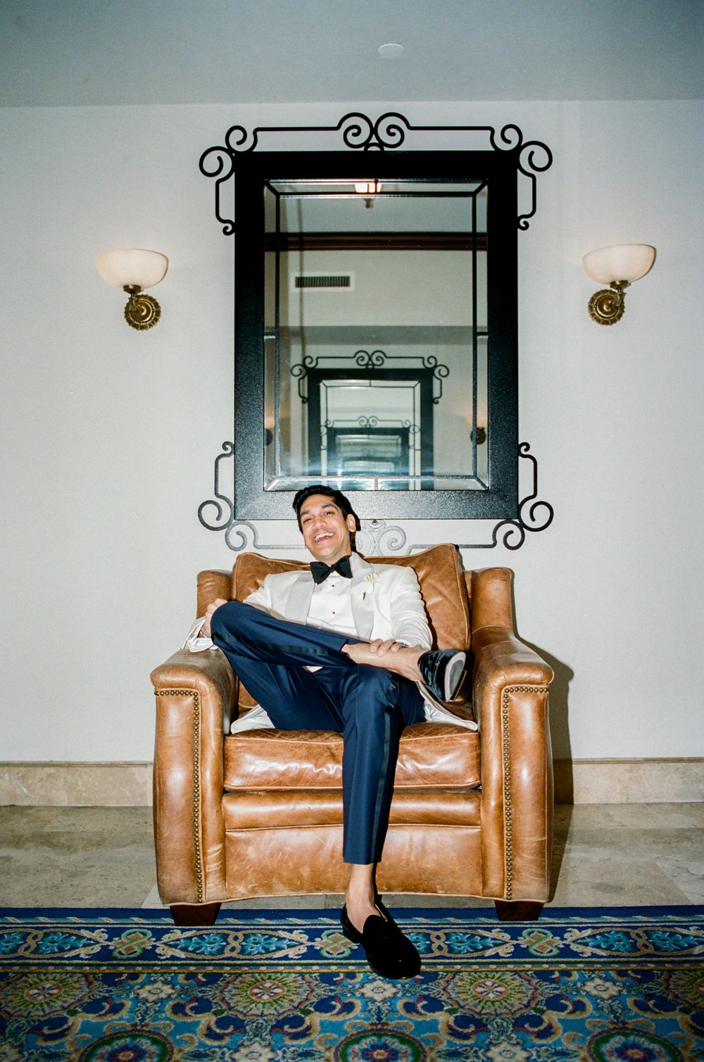 A sequence of relaxed poses on a brown leather armchair against a light wall with decorative sconces.