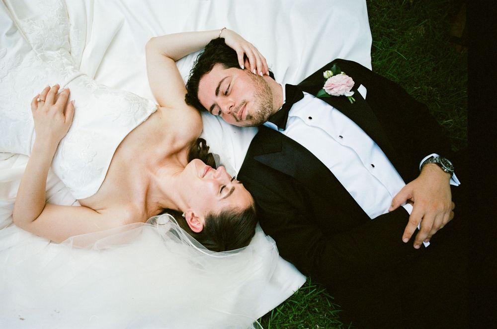 Bride and groom lying on grass in wedding attire, sharing a romantic moment on their wedding day.