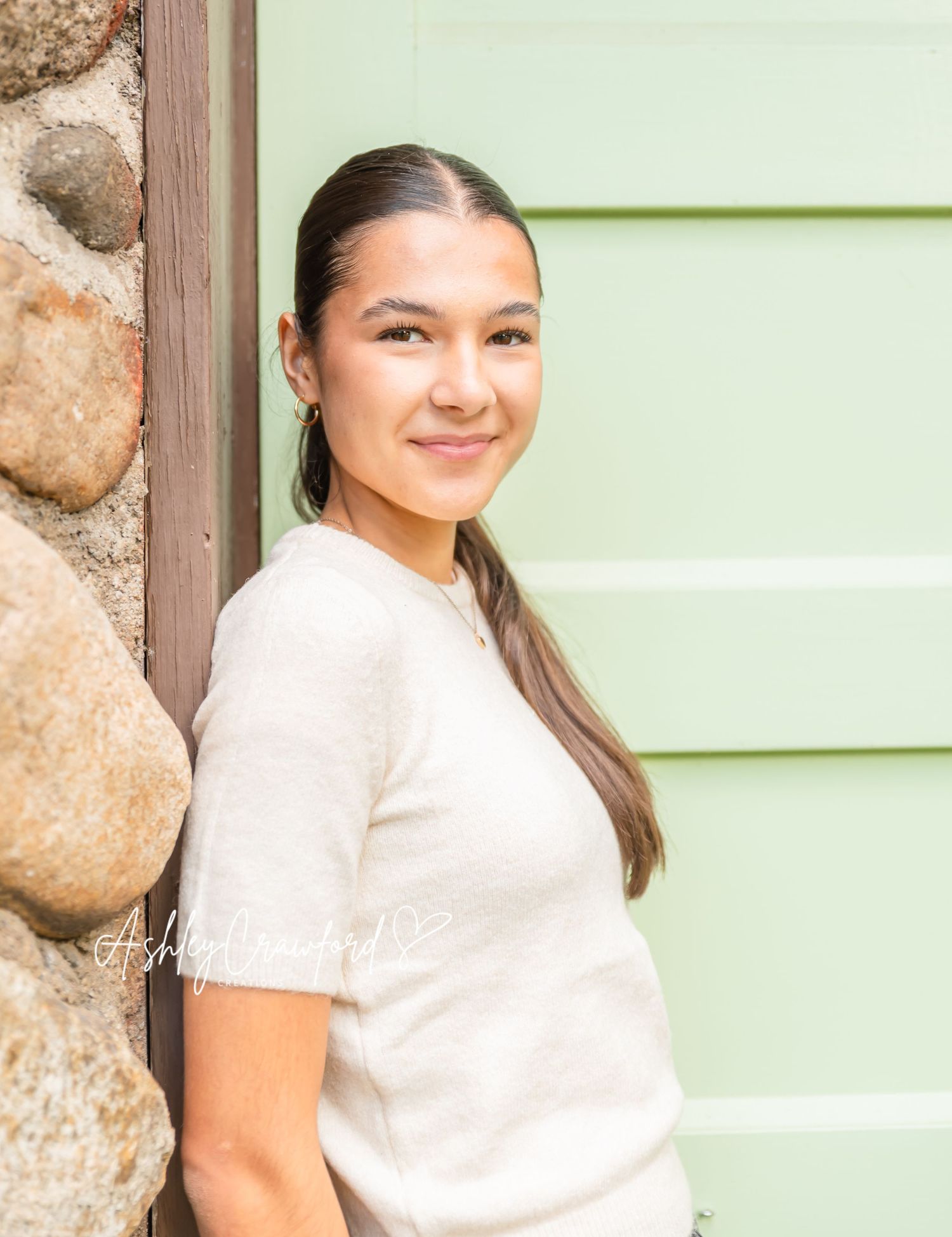 A portrait against a mint green wall and stone facade in natural light.