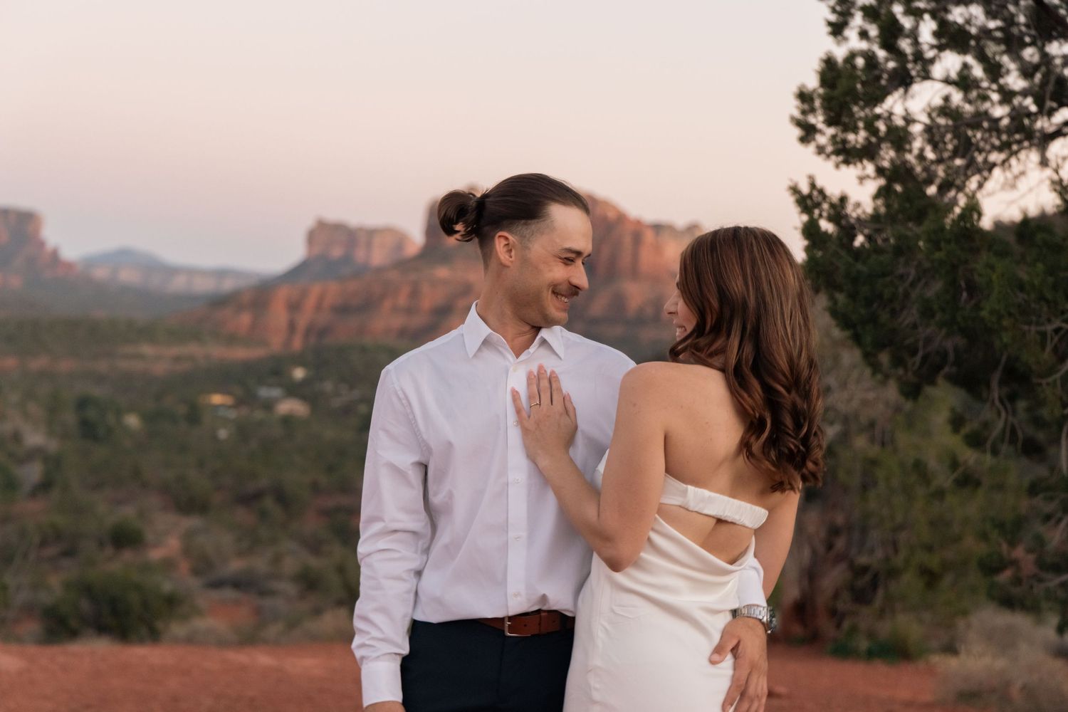 A couple in wedding attire share an intimate moment against the backdrop of red rock formations in Sedona at sunset.