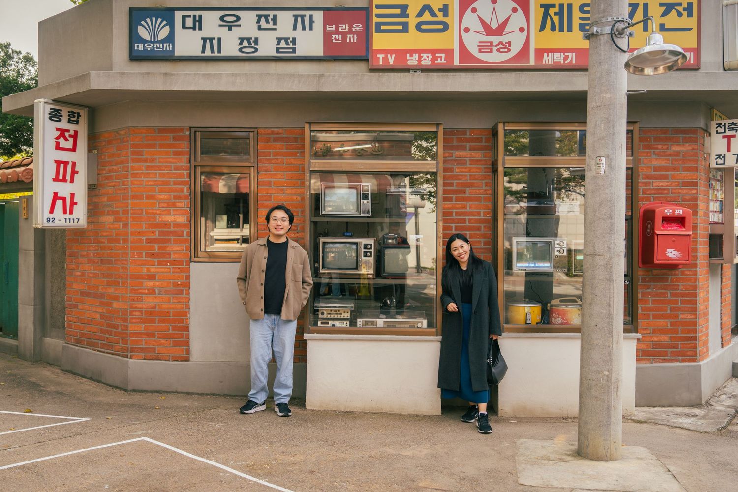 Korean storefront signs and advertisements line a commercial street with red brick buildings and pedestrians walking.