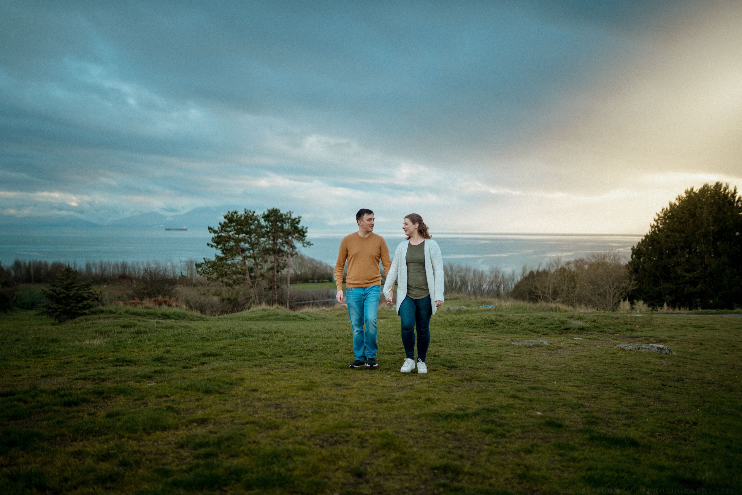 People enjoying a scenic sunset view on a grassy hillside overlooking a coastal landscape.