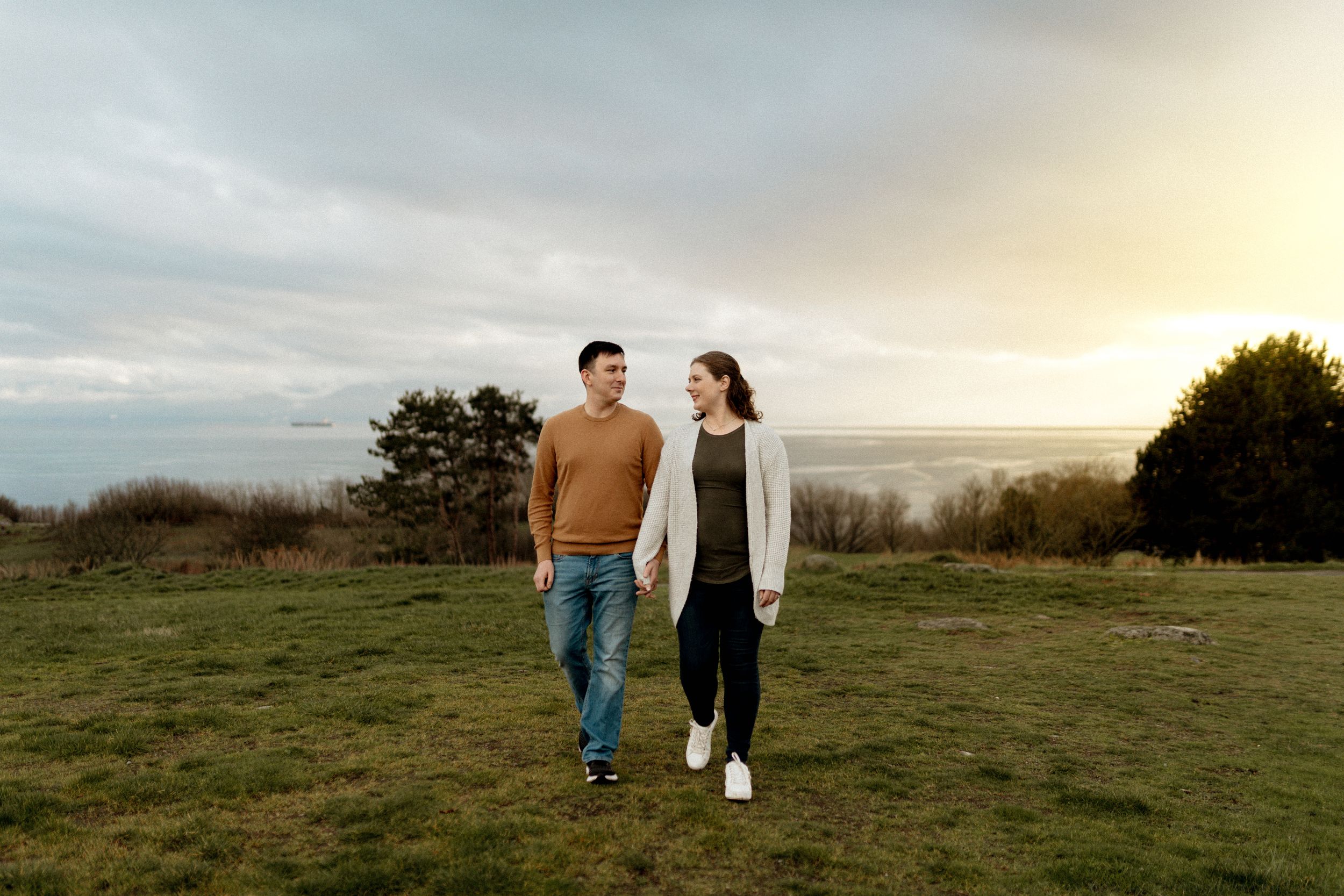 Two people walk hand in hand across a grassy hilltop against a moody sunset sky.