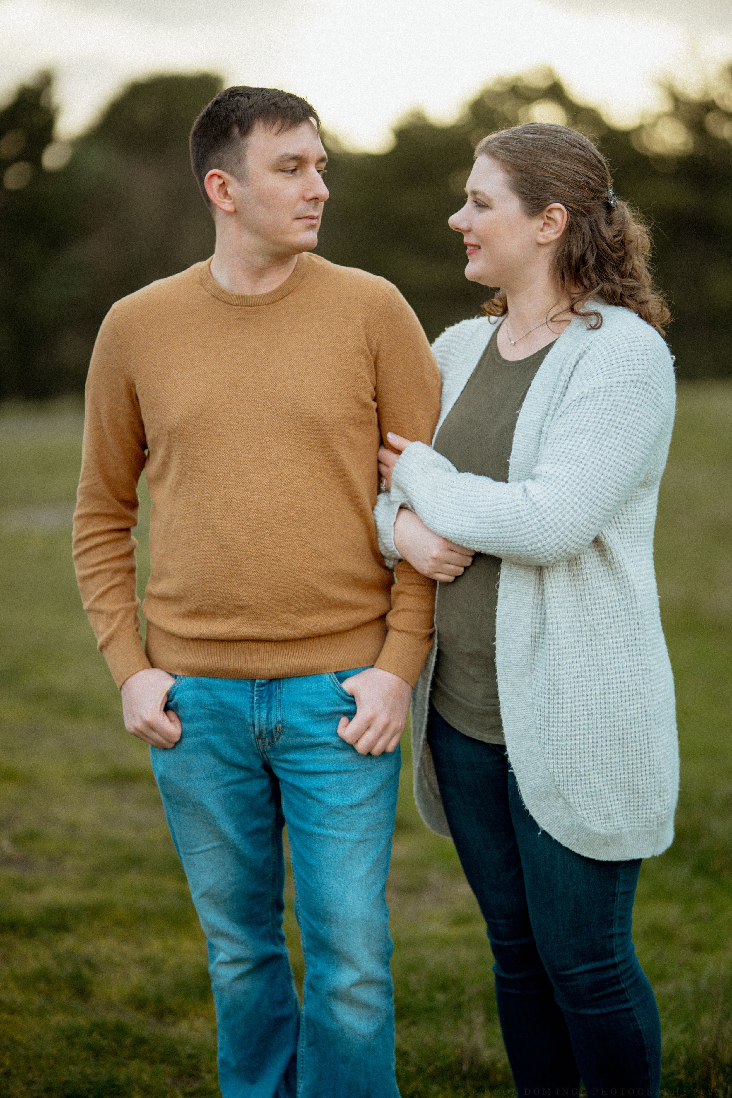 A couple in casual sweaters share tender moments together outdoors during golden hour.