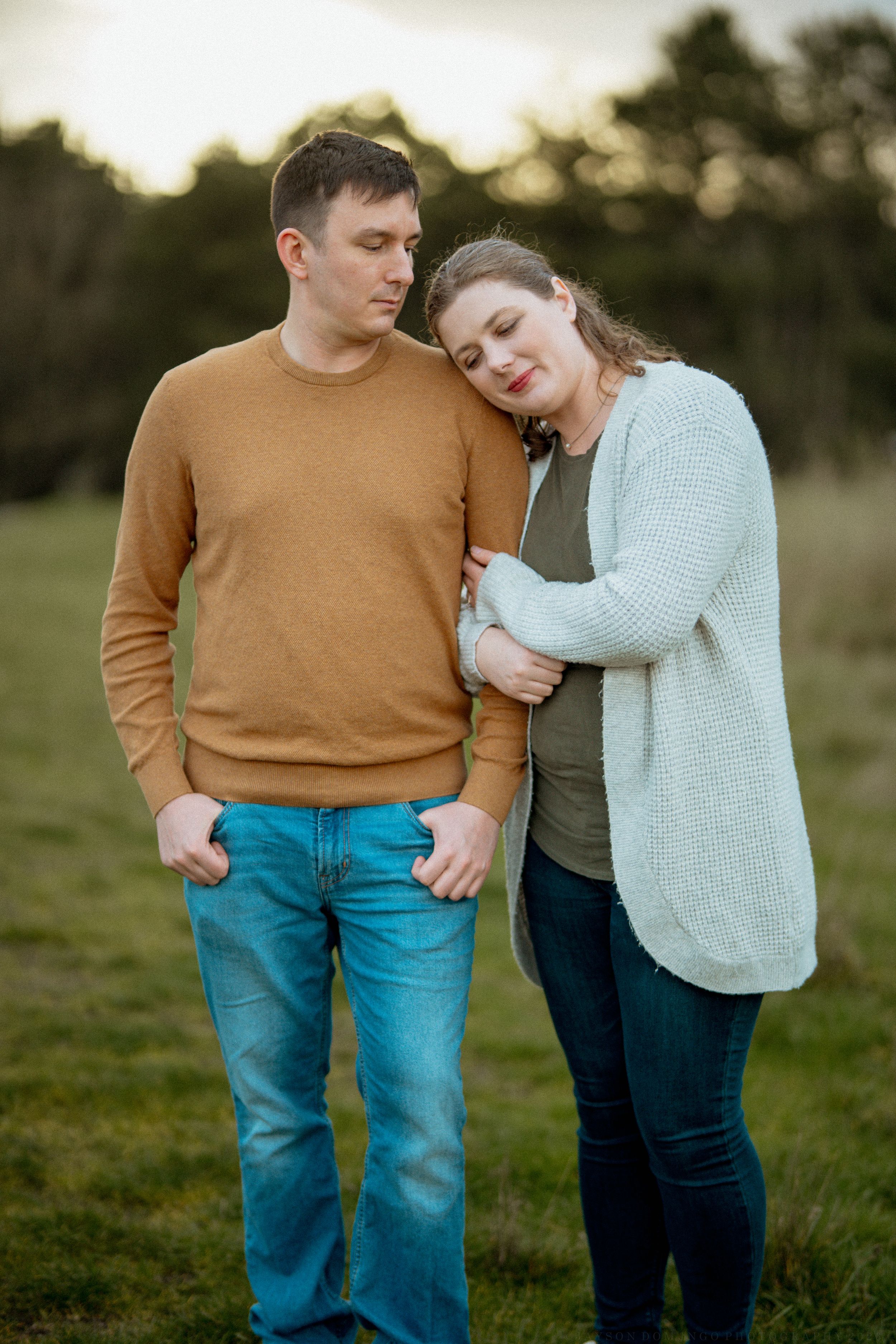 A couple in casual attire sharing an intimate moment outdoors at sunset in a grassy field.
