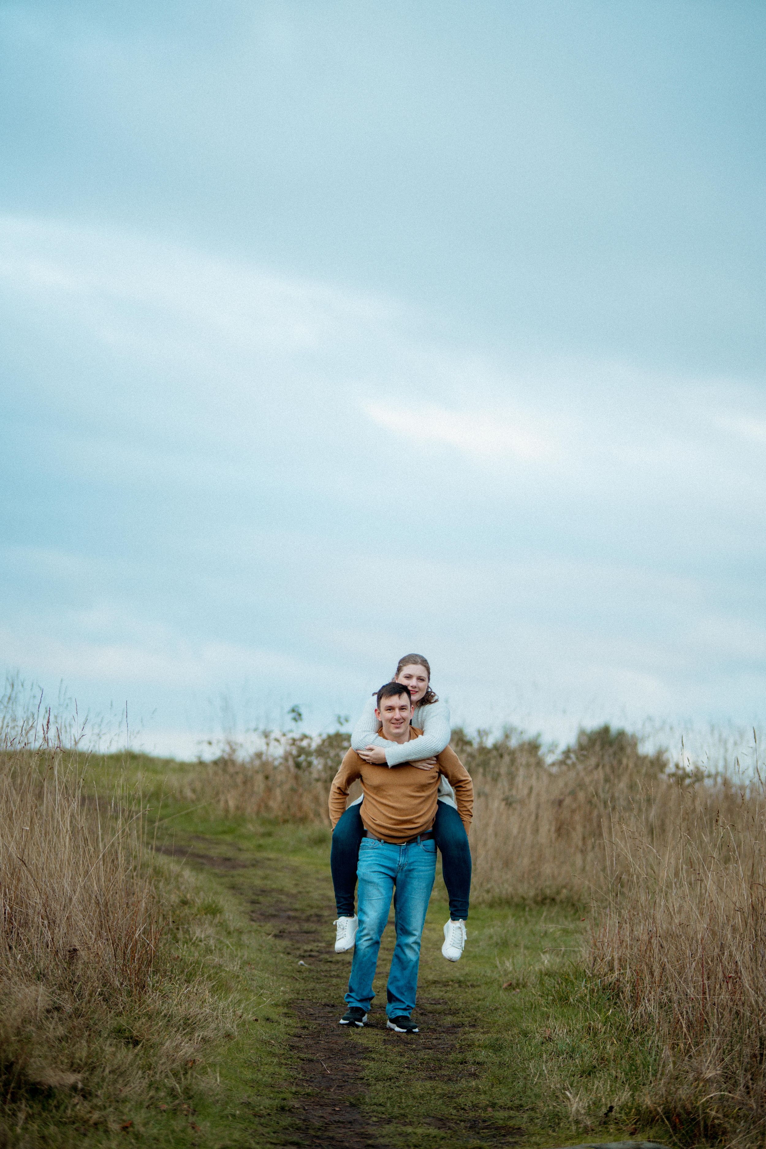 A playful sequence showing a person in blue pants and tan sweater bending down on a grassy hilltop path.