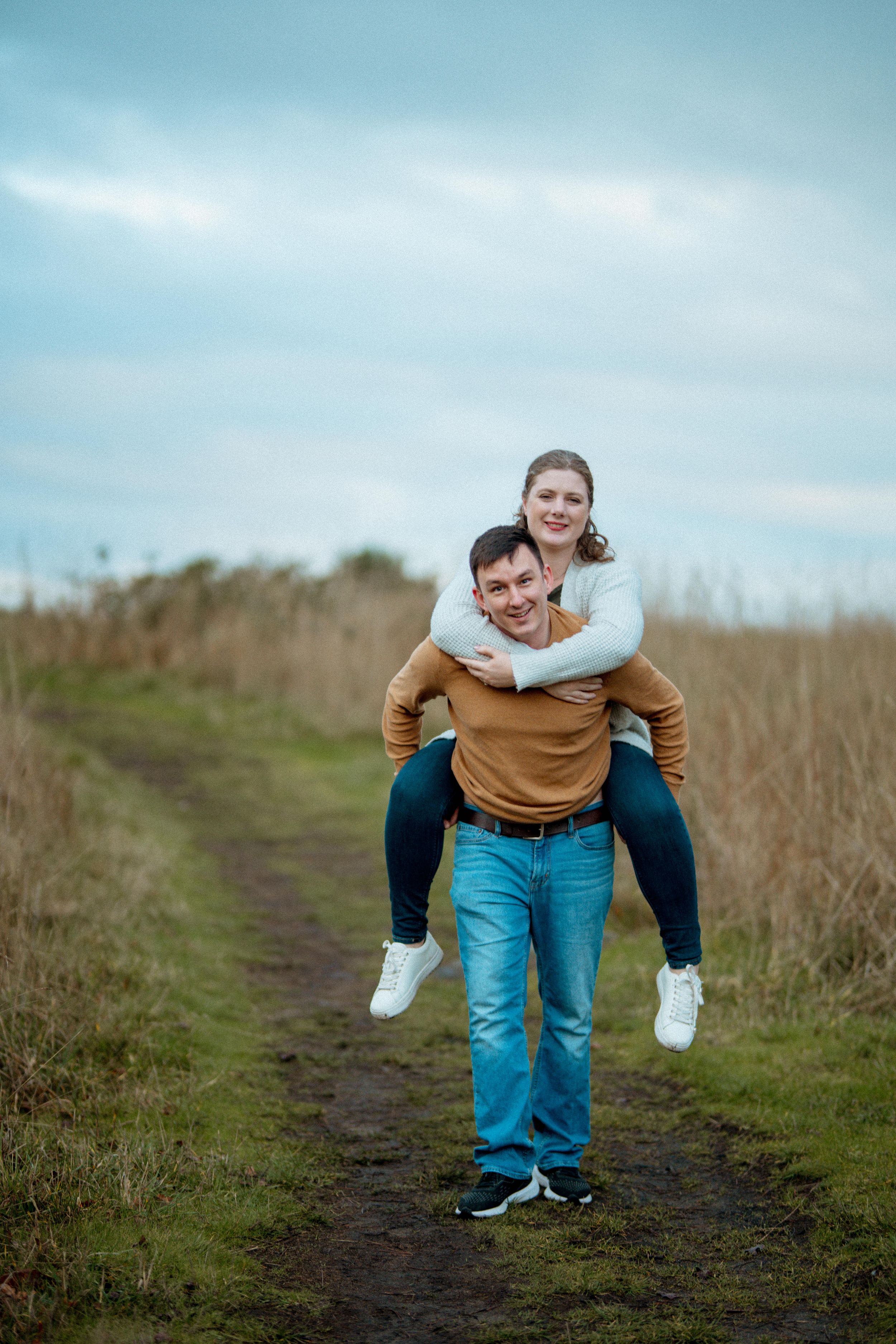 A playful sequence of two people having fun on a grassy trail against a cloudy sky.