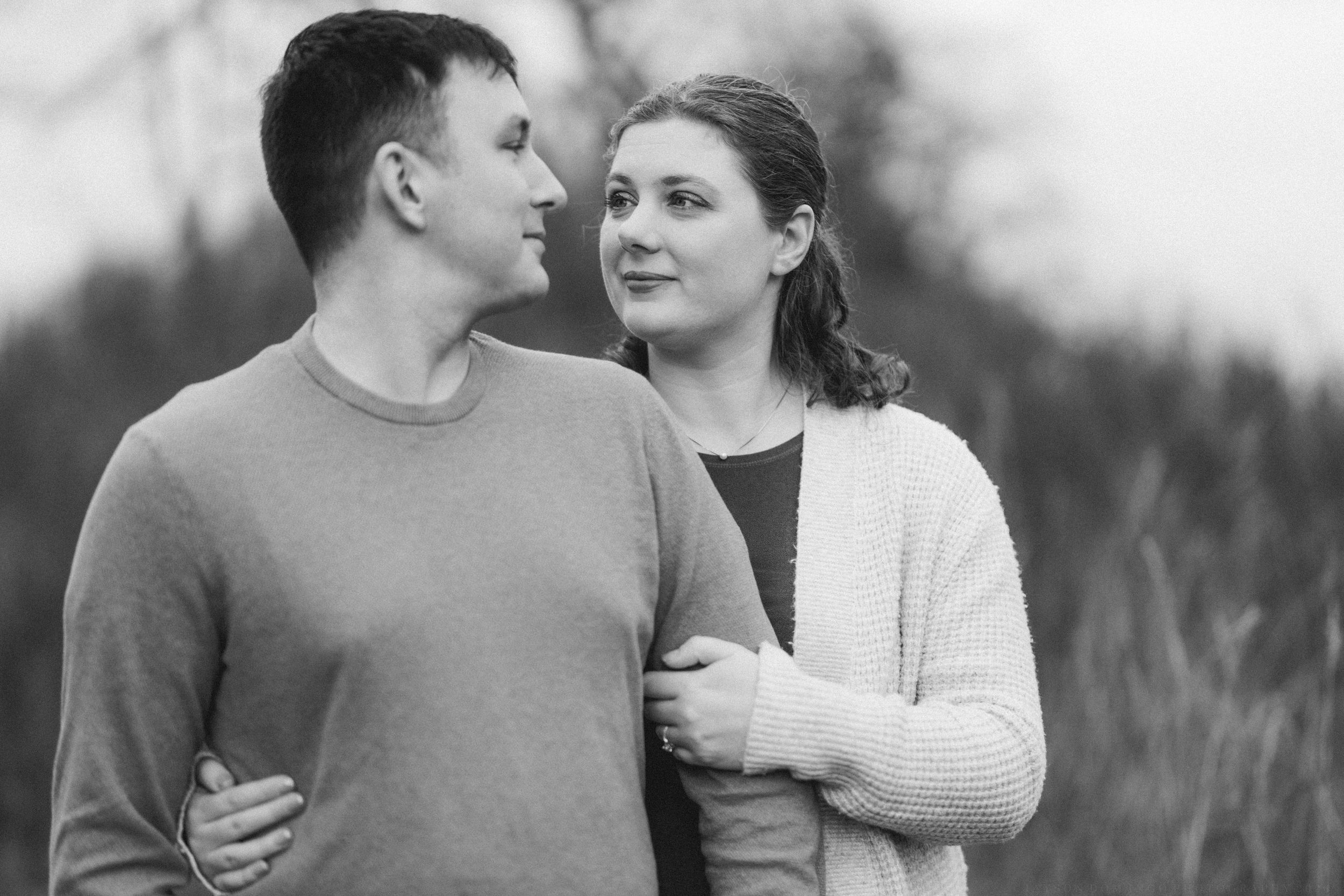 A romantic black and white portrait of a couple in casual sweaters gazing at each other outdoors.