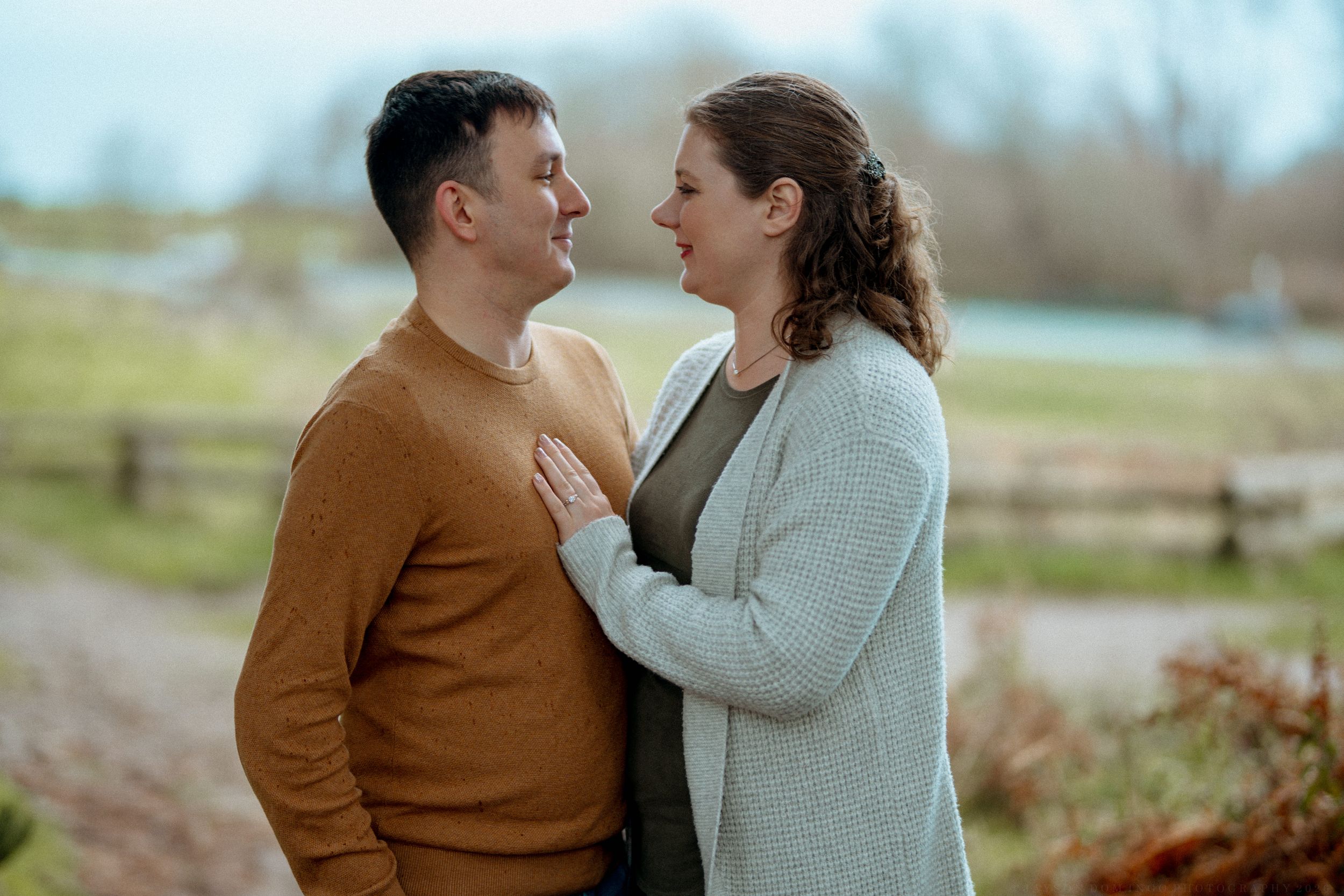 A couple in brown and gray sweaters share tender moments outdoors during an autumn photoshoot.