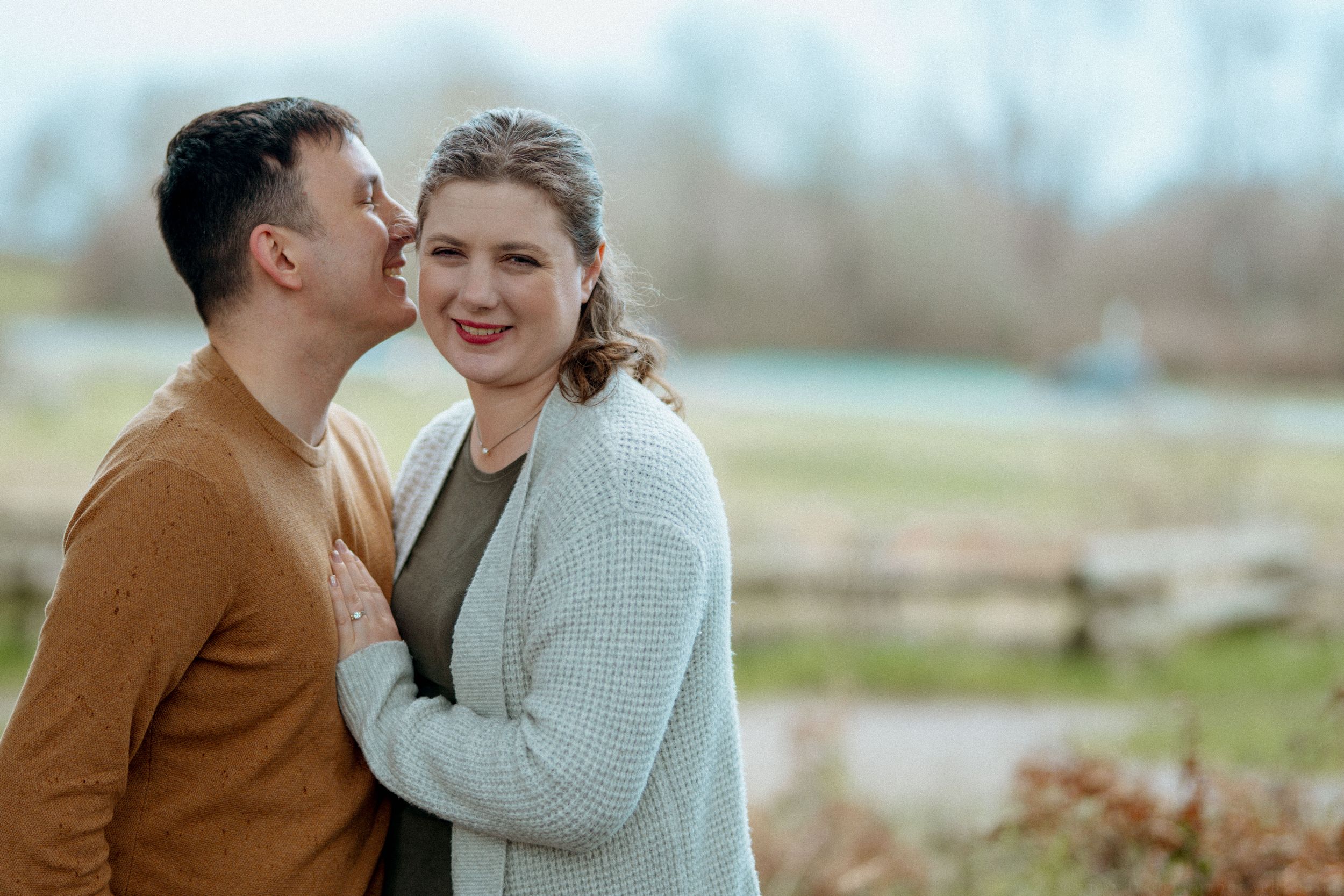 A couple shares a tender moment outdoors on an autumn day, wearing cozy sweaters against the cool weather.