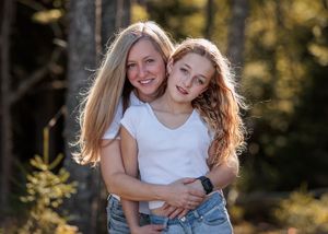 Two people embracing in a sunlit forest setting with golden light filtering through the trees.