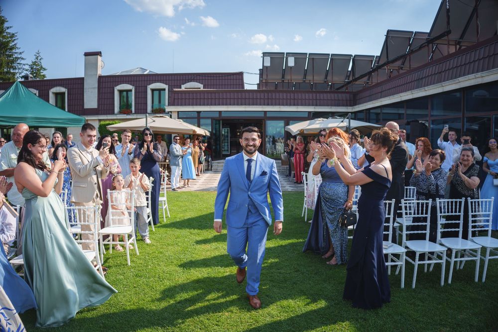 Wedding guests mingle and socialize on a green lawn outside a venue on a sunny summer day.