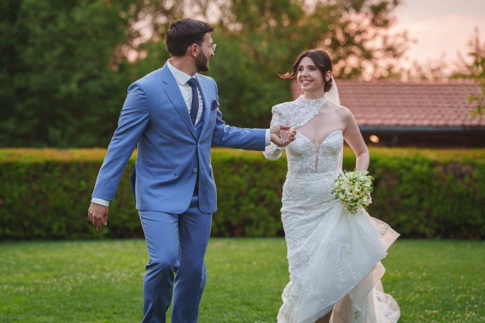 Couple in formal wedding attire walking together on a lush green lawn during golden hour.