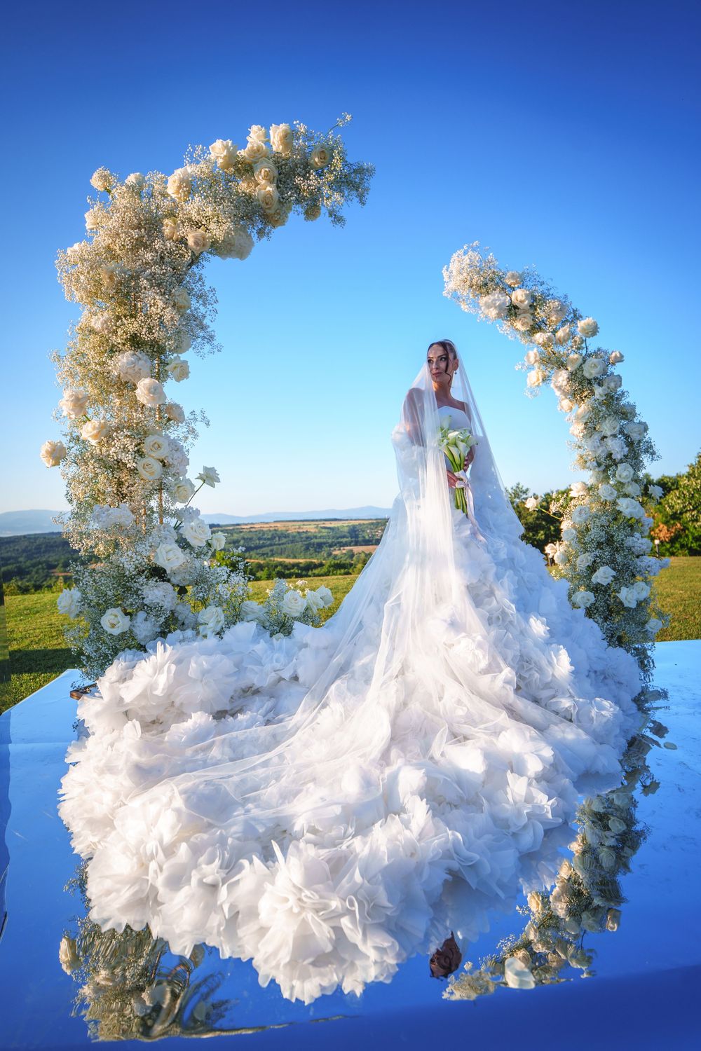 A stunning wedding scene with a floral arch and flowing white gown against a scenic countryside backdrop.