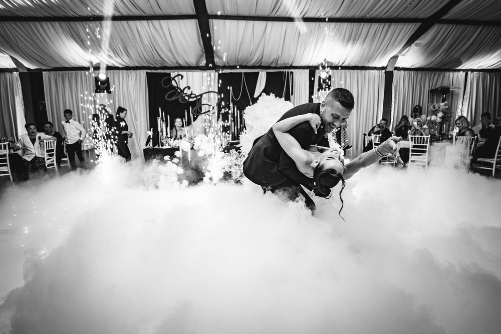 A couple shares their first dance at a wedding reception with fog machines creating a dreamy atmosphere on the dance floor.