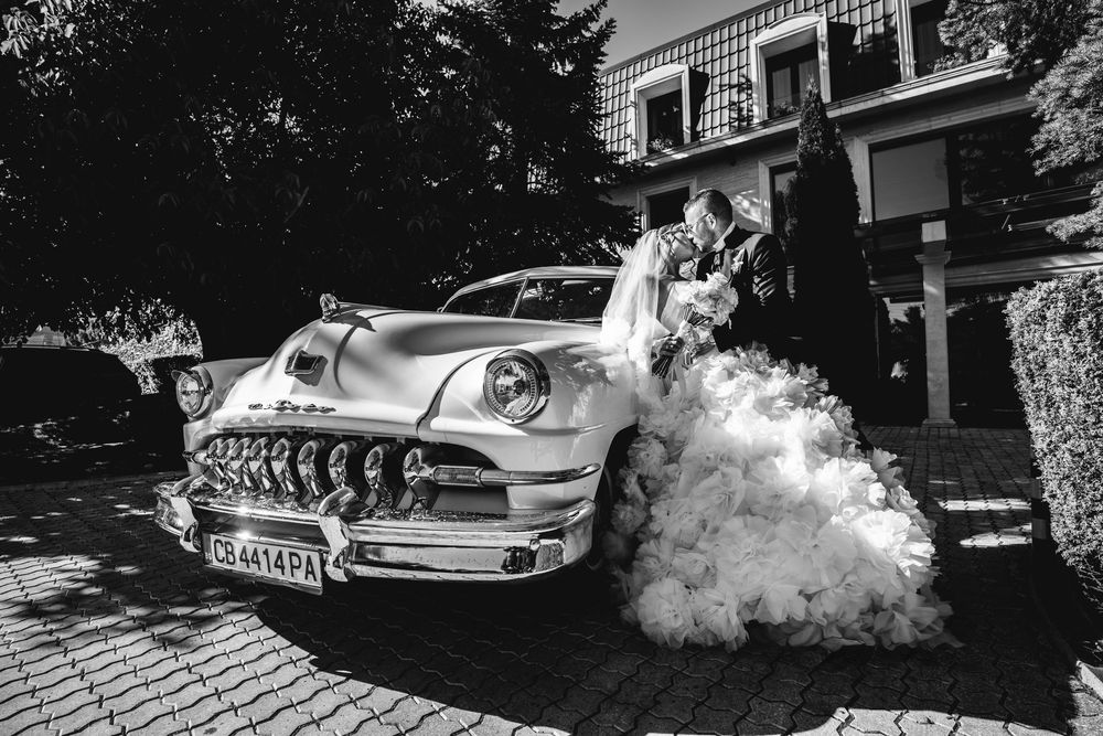 Black and white photo of classic cars parked along a street with smoke or fog creating a moody atmosphere.