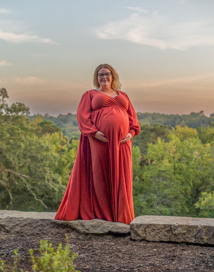 pregnant woman standing on a ledge with a beautiful sky in the background