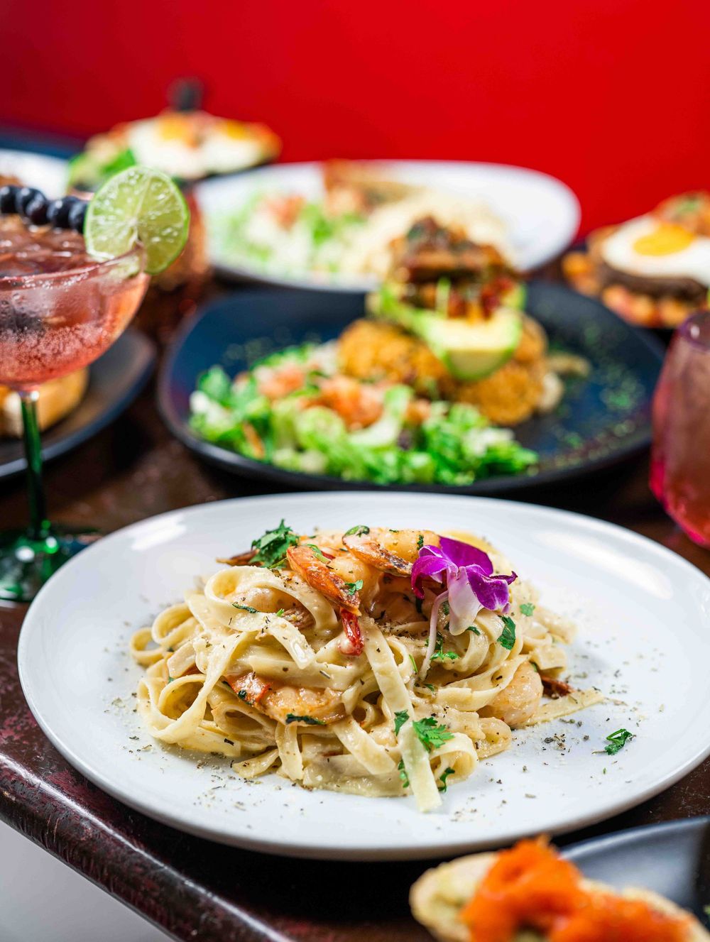 Fettuccine pasta dish garnished with herbs and served on white plates against a vibrant red background.