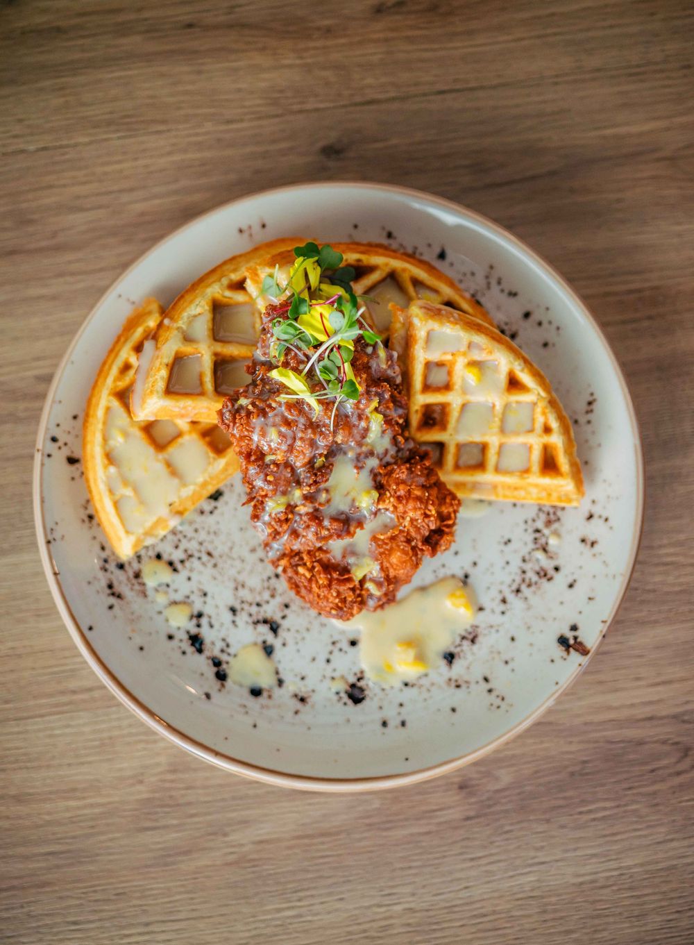 A sequence of plated dishes showing crispy golden waffles paired with breaded chicken and garnished with herbs and crumbs.