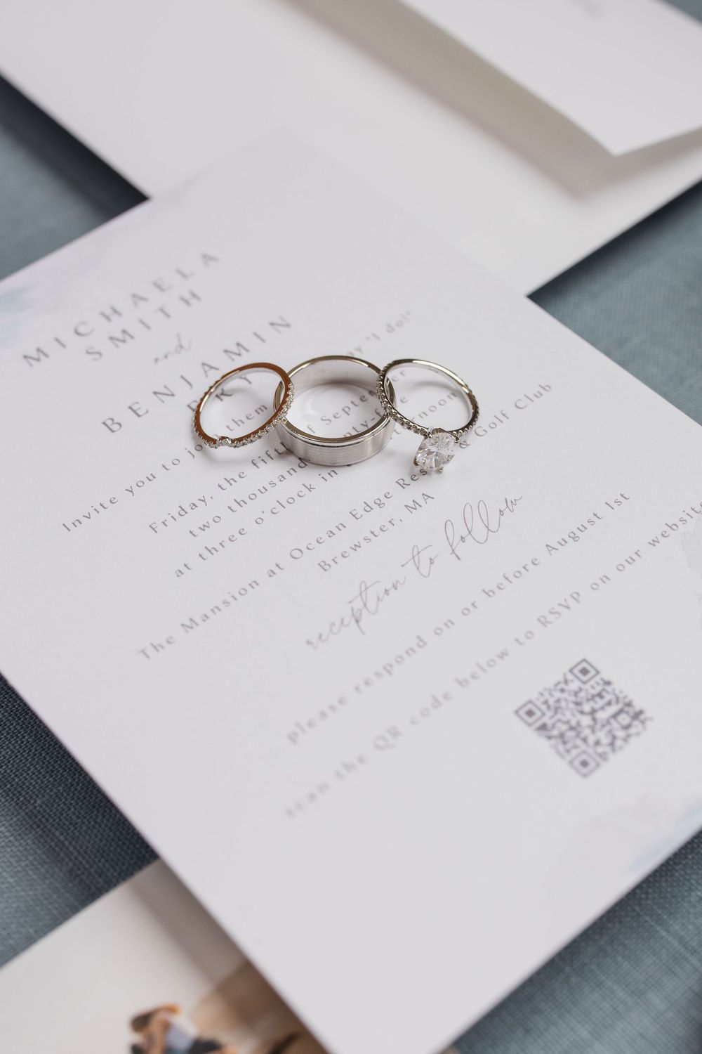 Wedding rings and diamond engagement ring displayed on elegant white invitation with QR code.