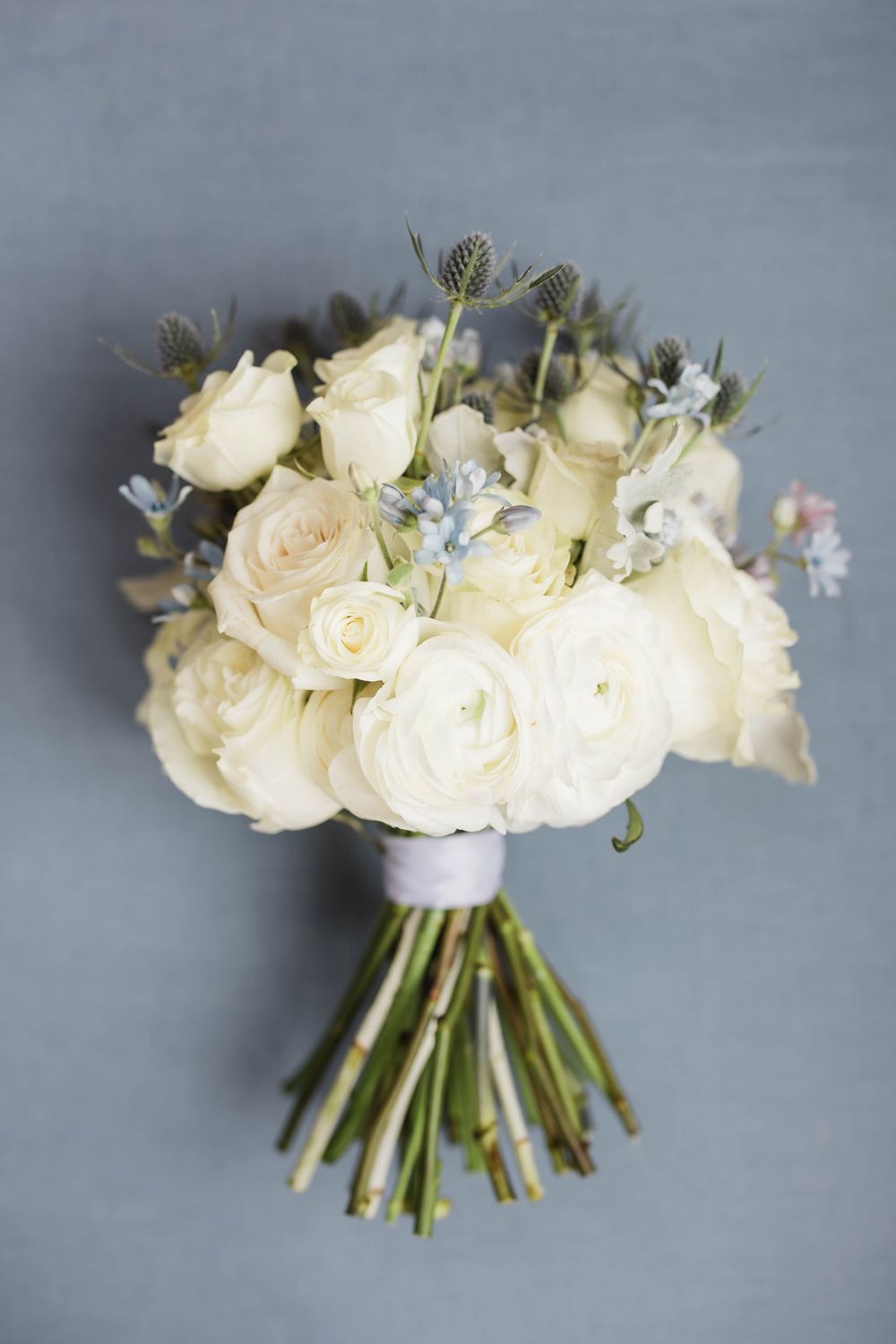 A series of elegant white rose and ranunculus bridal bouquets with pale blue accents against a gray background.