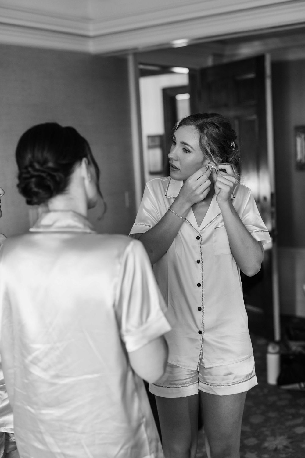 People in white attire helping each other get dressed and make final preparations in a hallway.