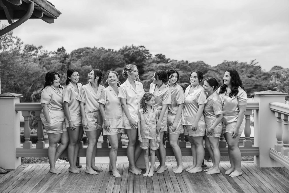 Group of women in matching gray robes pose together on wooden deck during cloudy day.