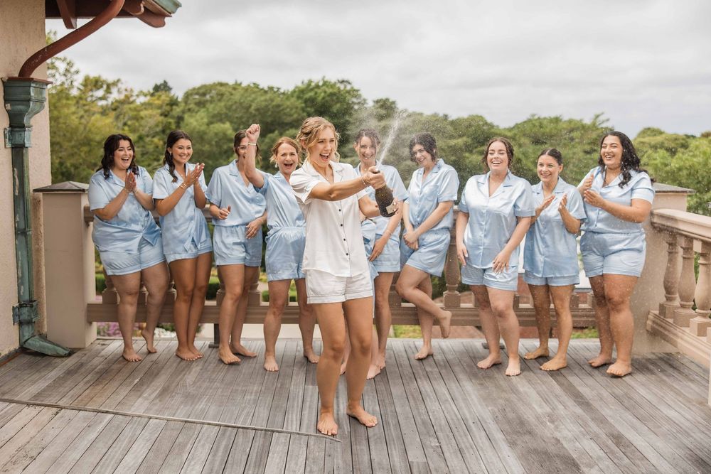 Group in matching light blue pajama sets poses together on wooden deck during celebration event.