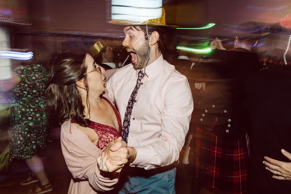 A couple shares a romantic dance moment at a nighttime party with motion blur and colorful lights in the background.