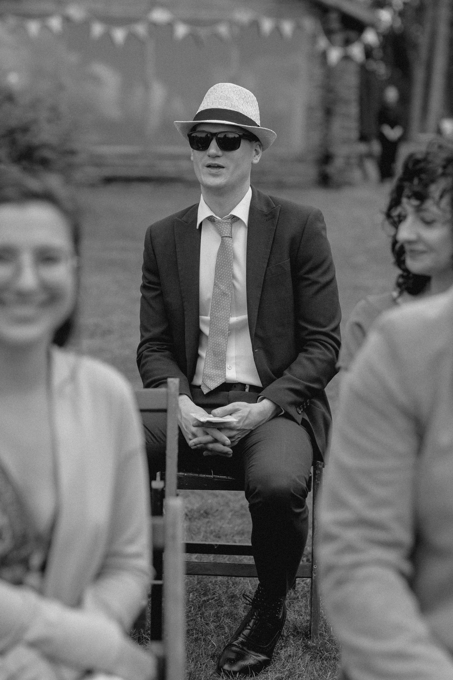A person in a suit and hat sits on a stone ledge in a black and white photograph.