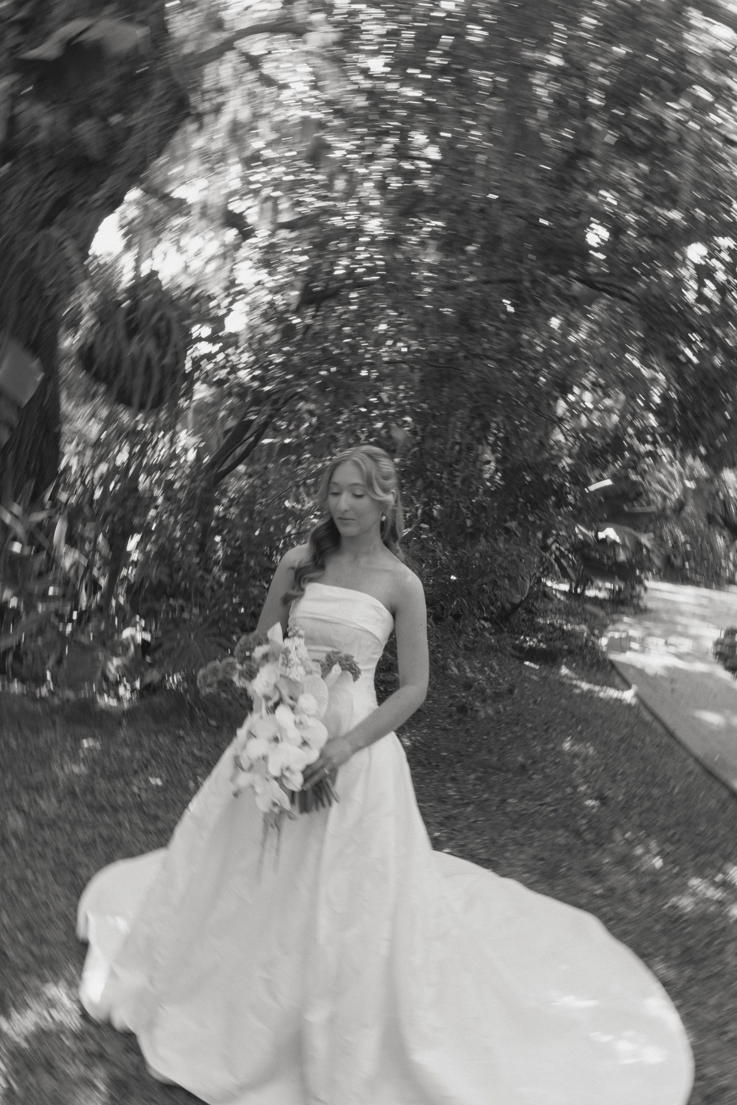 A bride in a flowing white wedding dress twirls gracefully in a garden setting, creating a beautiful spinning motion.
