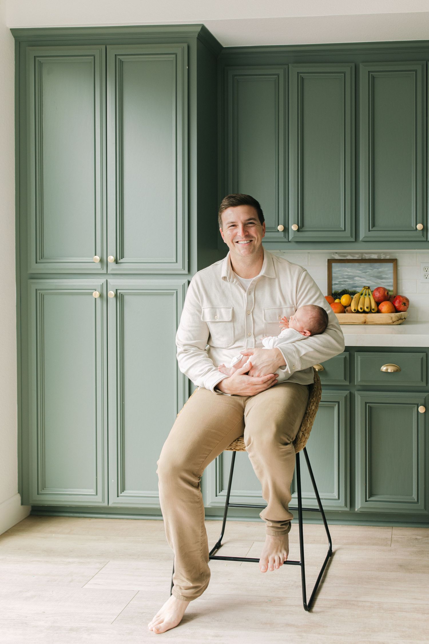 Three children in matching dresses lounge playfully across green kitchen cabinets with brass hardware.