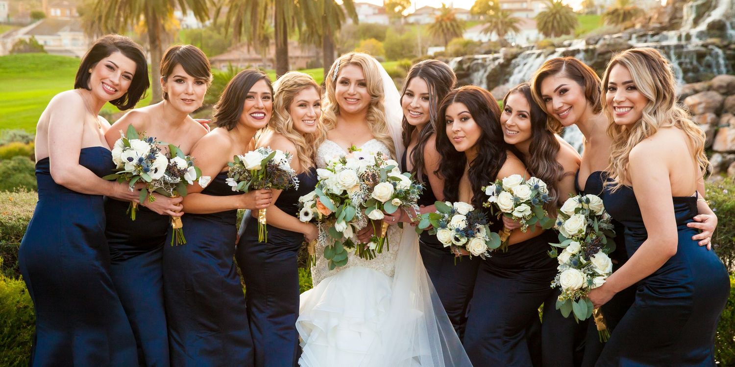 Wedding party poses together outdoors with palm trees and white floral bouquets at sunset.