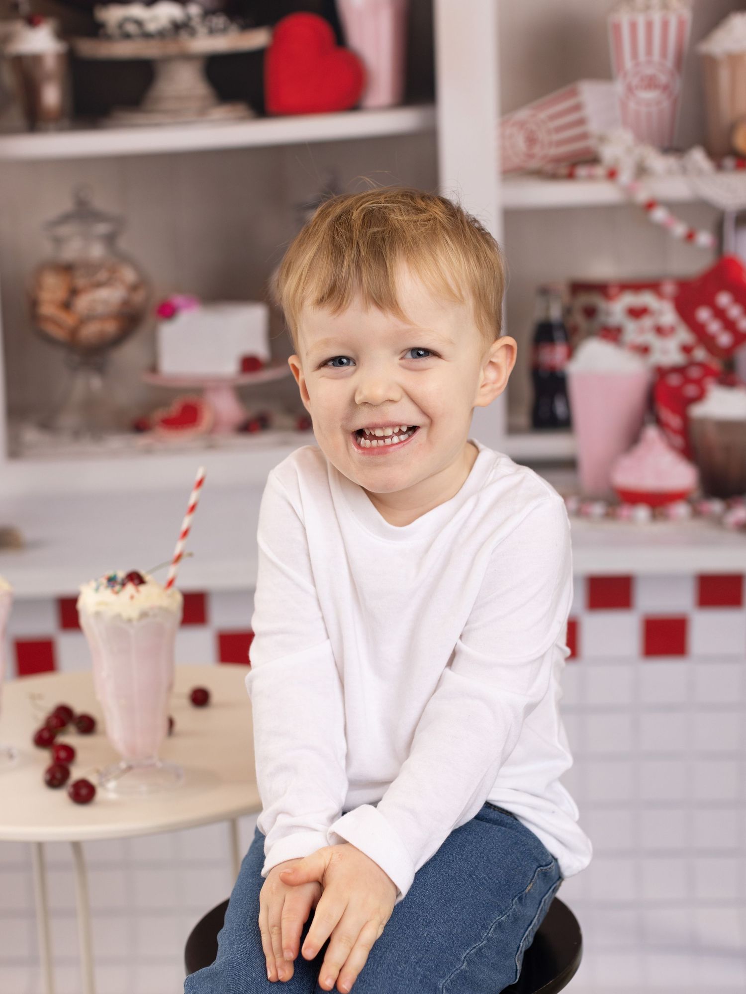 Child in white shirt and jeans sitting in festive red and white kitchen setting with holiday decorations.