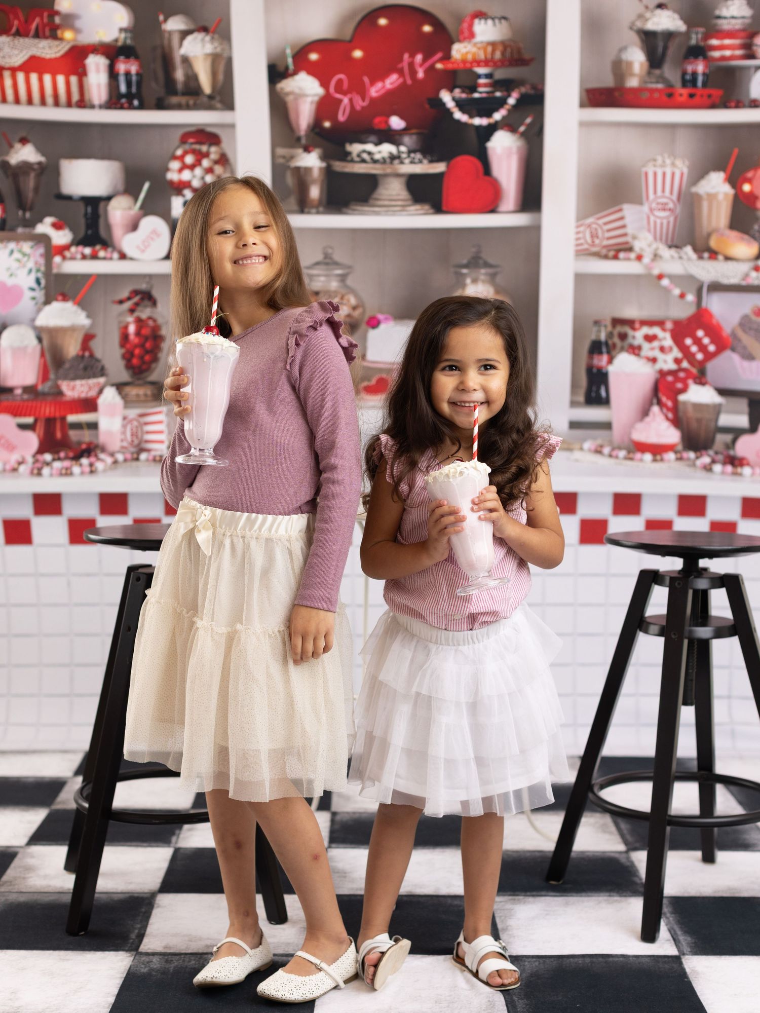 Children in white dresses twirling and dancing in a retro-styled diner setting with red and white decor.